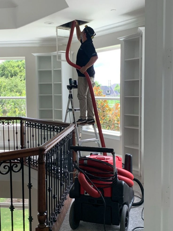 Technician accessing a ceiling vent with cleaning equipment